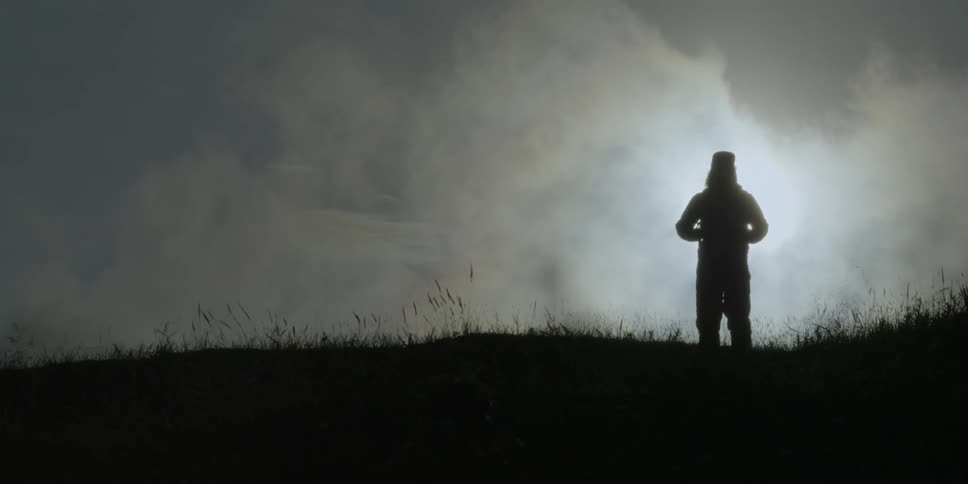 Silhouetted man stands in a grassy field
