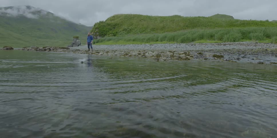 Man throws a rock into ocean and it skips across the top of the water