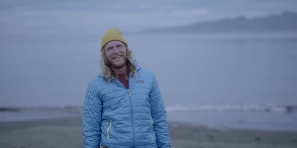 A man is smiling and laughing as he stands on a shoreline
