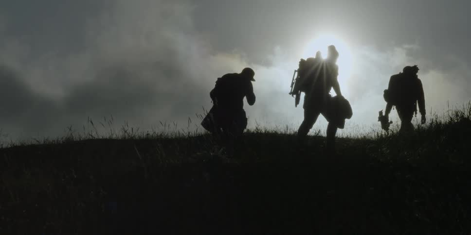 Silhouetted hikers climb a grassy hill