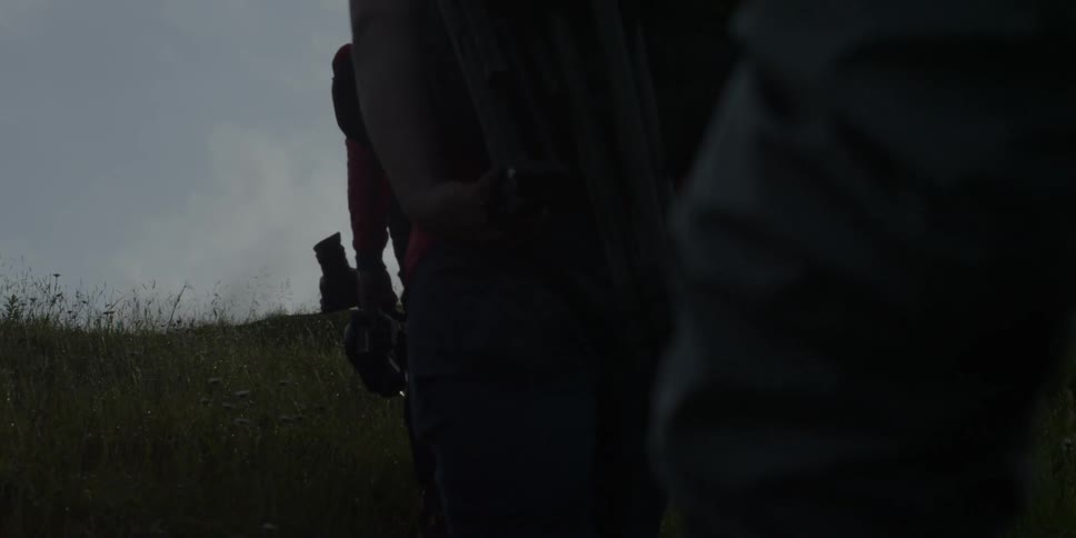 A group of people are walking up a hill carrying equipment during the day