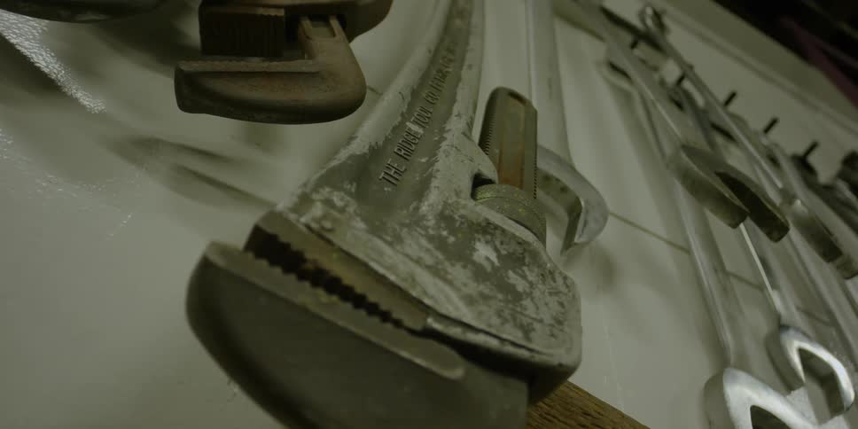 A large wrench sways from a hook on the wall