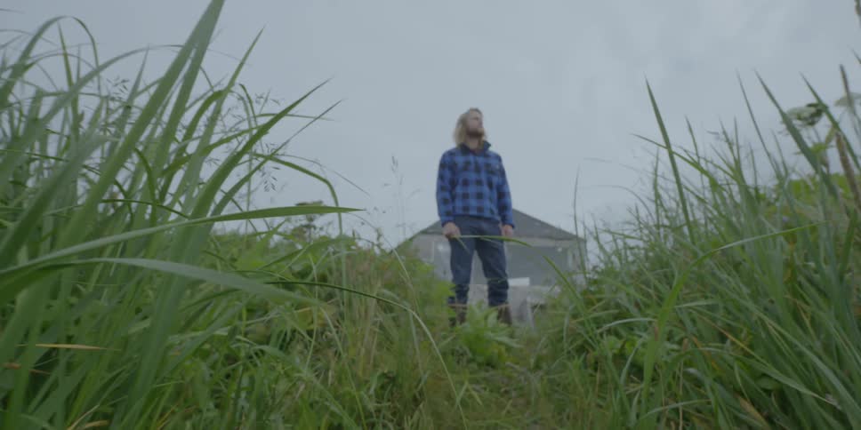 Man stands in tall grass near a cabin