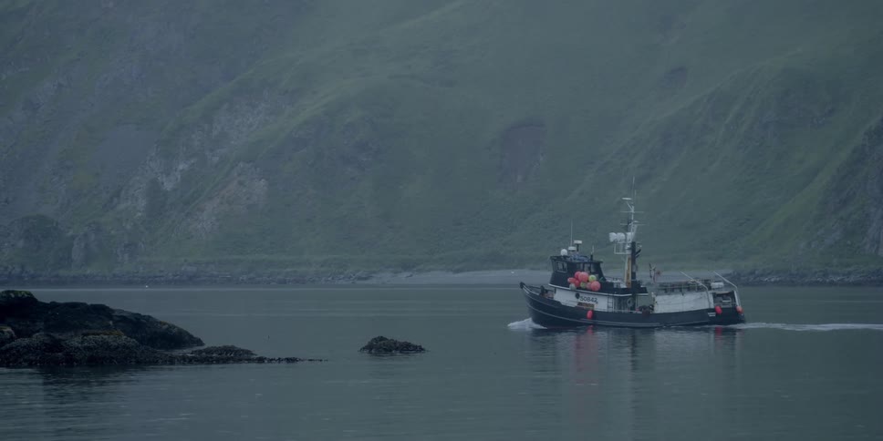 A boat moves along in the water near a mountain