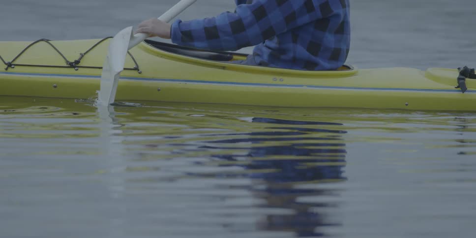 A person paddles a kayak with a shovel