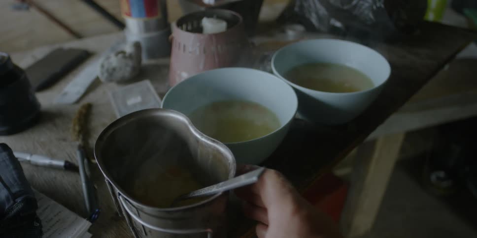 A person puts a spoon in a metal bowl of steaming soup
