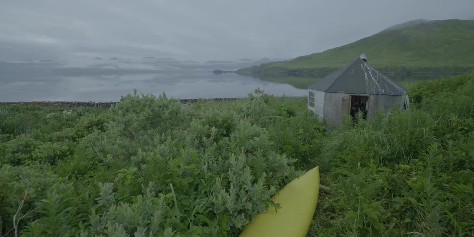 A kayak is overturned next to a shore side cabin