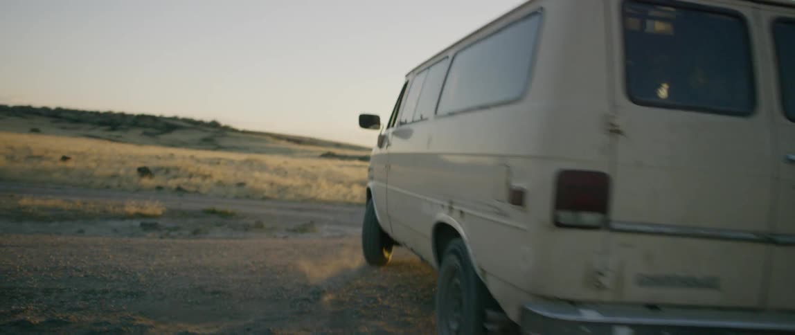 A man drives a van on a dirt road
