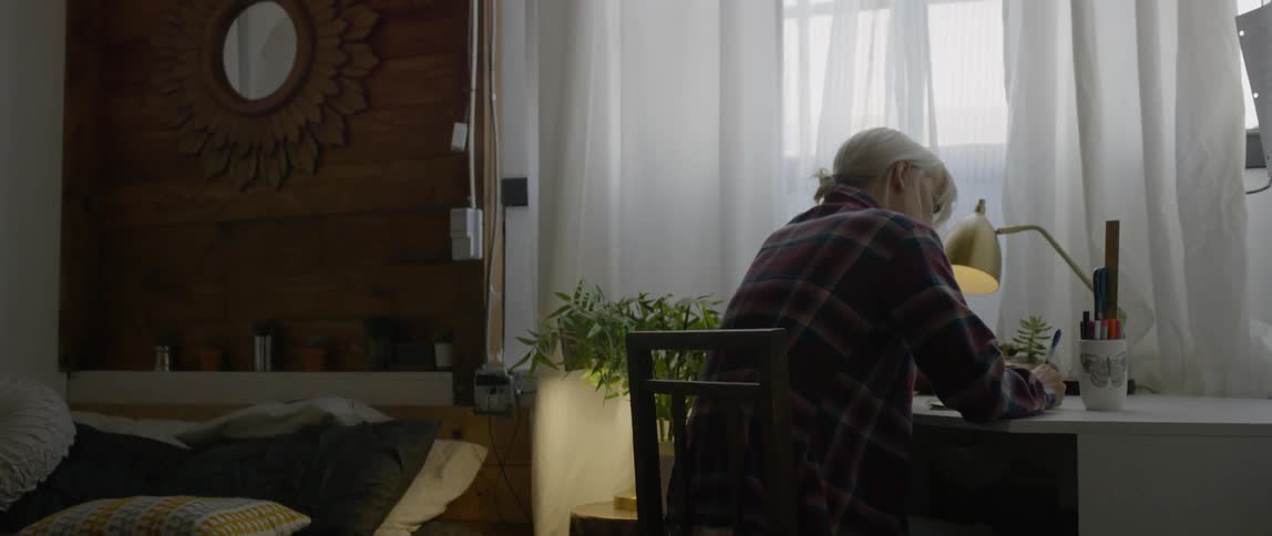 A woman writes at a desk in a bedroom