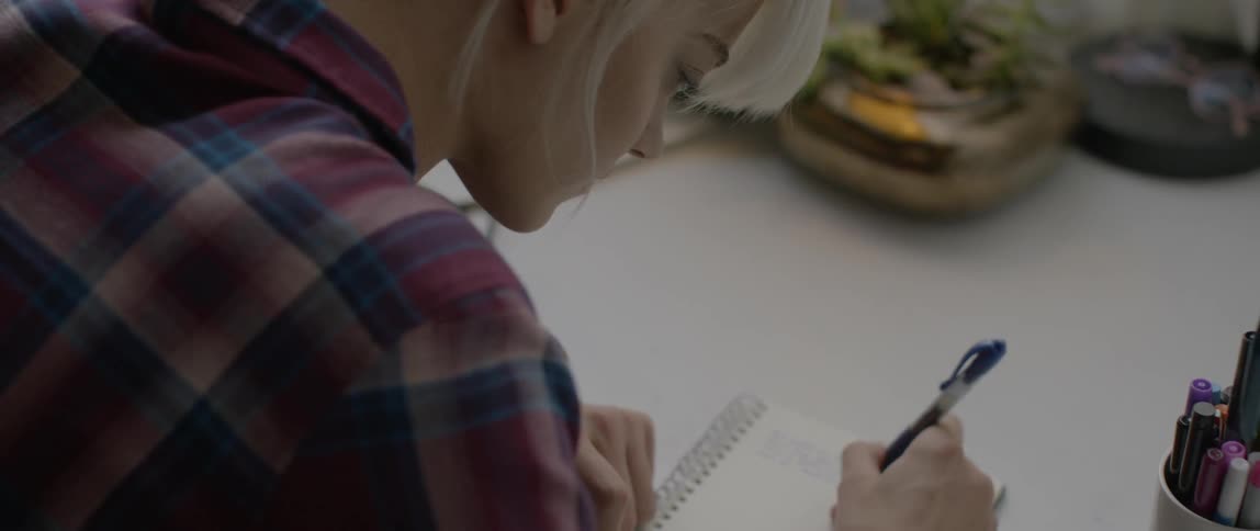 Woman writes on a small notepad on a white desk