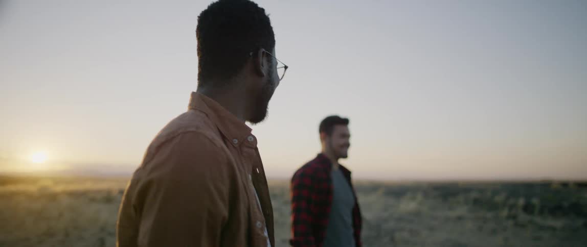 Two men are standing outside at dusk laughing and talking