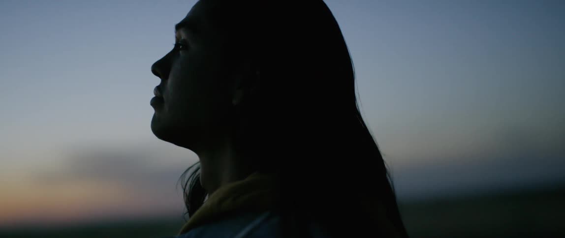 A long-haired person stares up at the sky