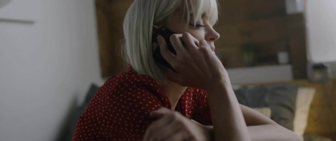 Woman sits at the edge of a bed and picks up a phone