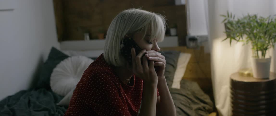 A woman sits down on a bed while talking on the phone