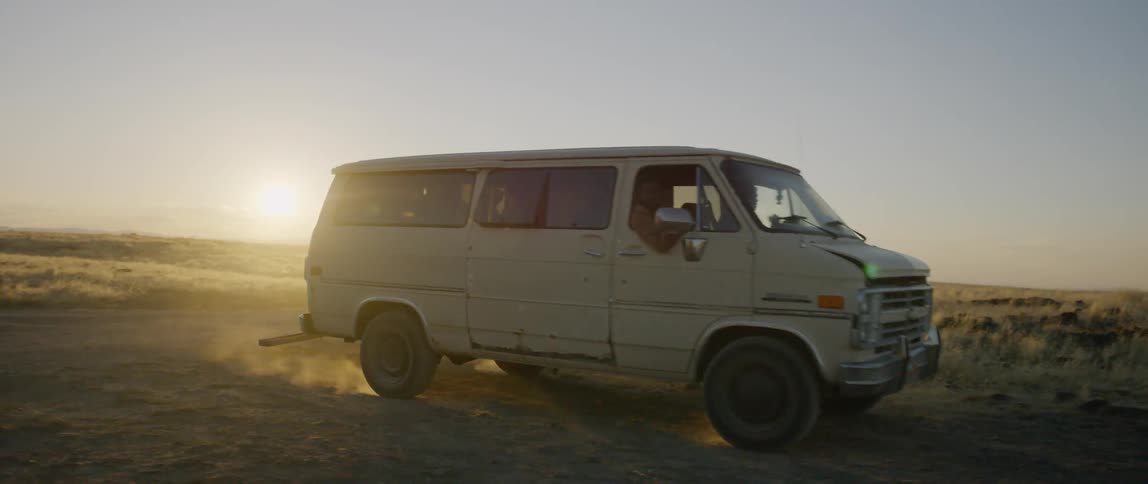 A van drives in a rural field at sunset