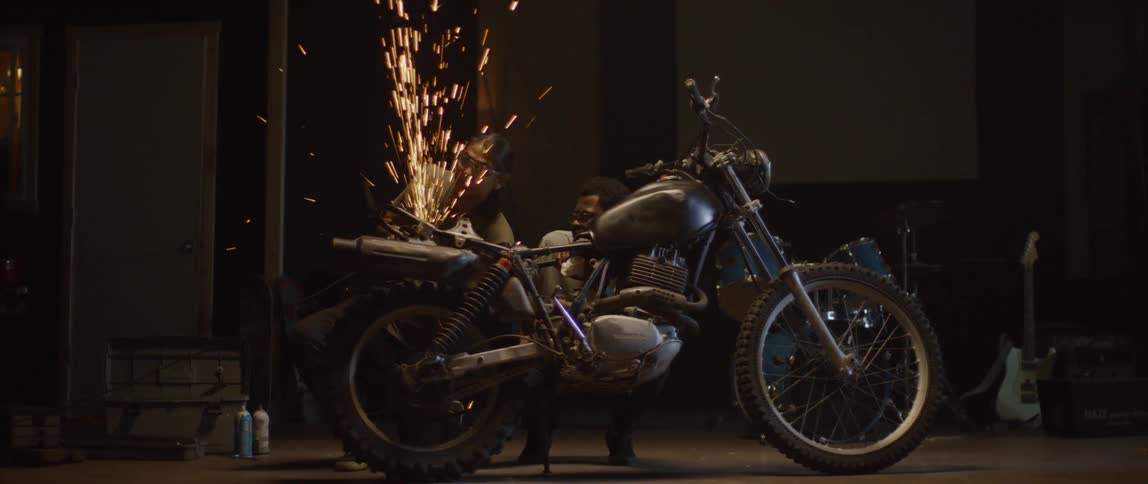 A man is welding a piece on a motorcycle while another looks on
