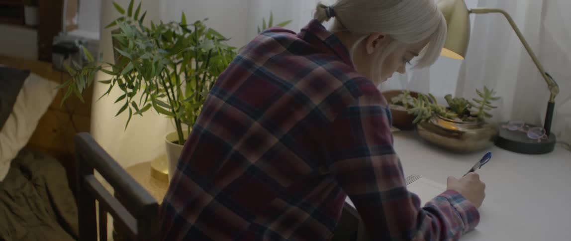 A woman writes at a desk in a bedroom