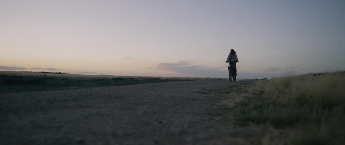 Person rides a motorcycle on a rural dirt road at dusk