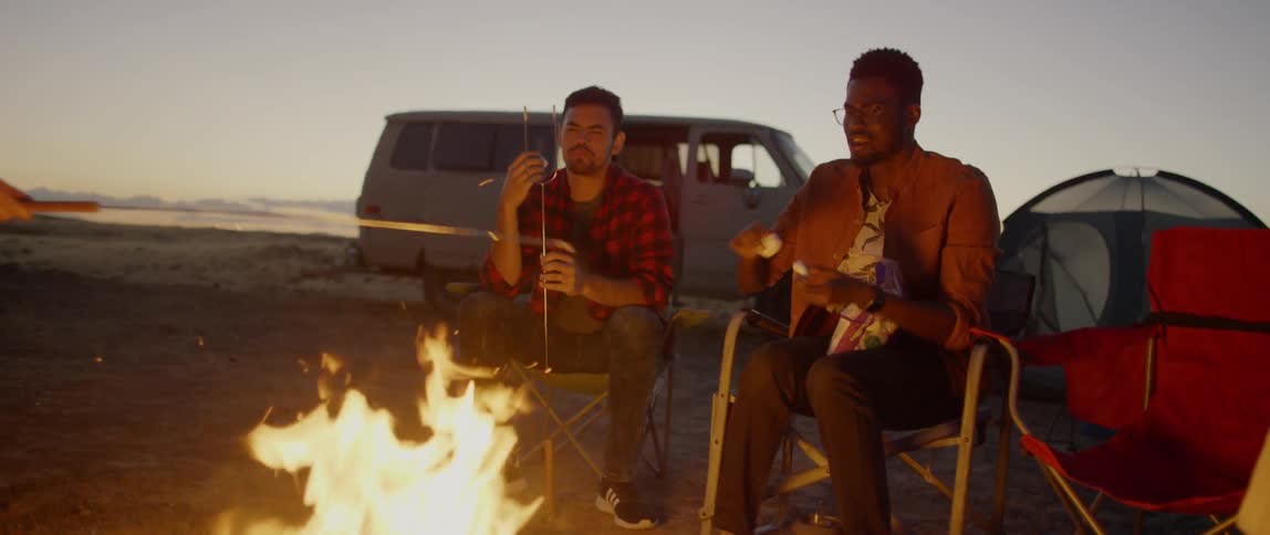 Friend roast marshmallows over a campfire at sunset