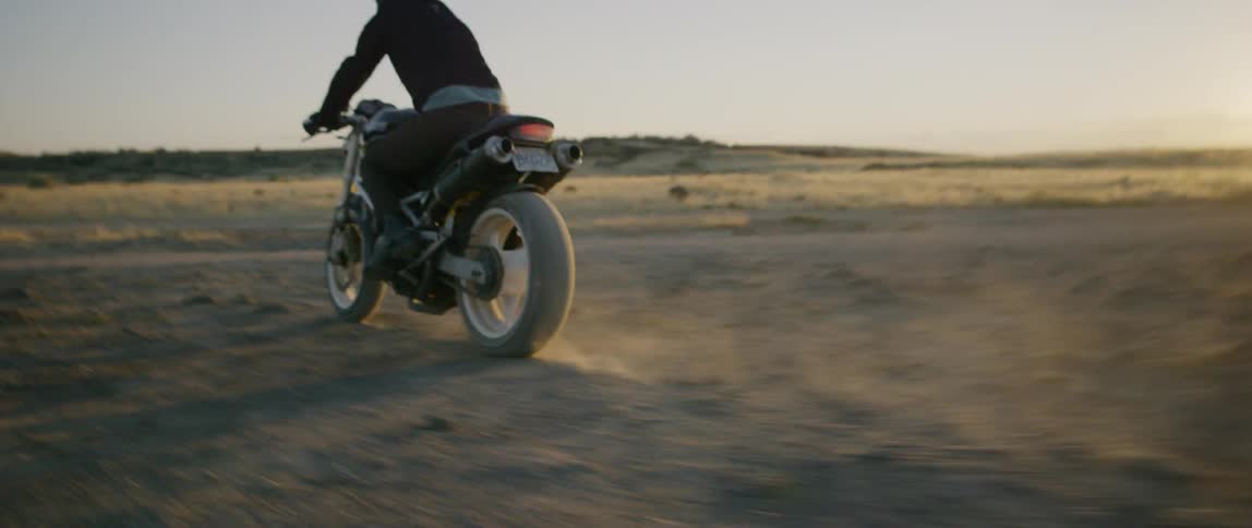 A motorcyclist rides across a rural dirt field at sunset