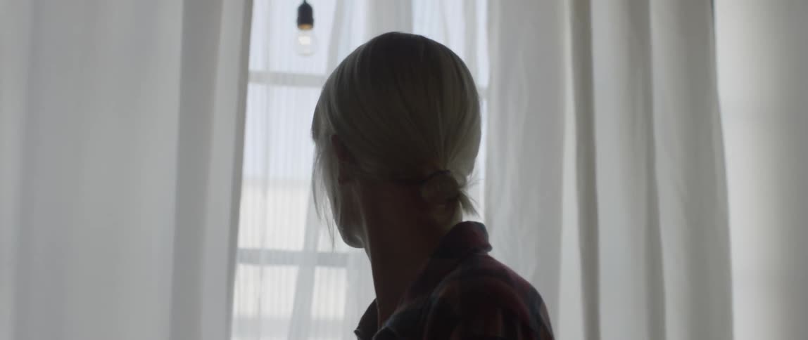 A woman standing in a room is looking toward a window during the day
