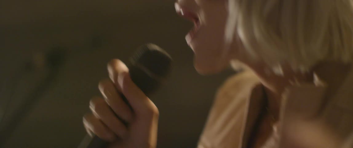 A woman sings into a microphone and claps her hands