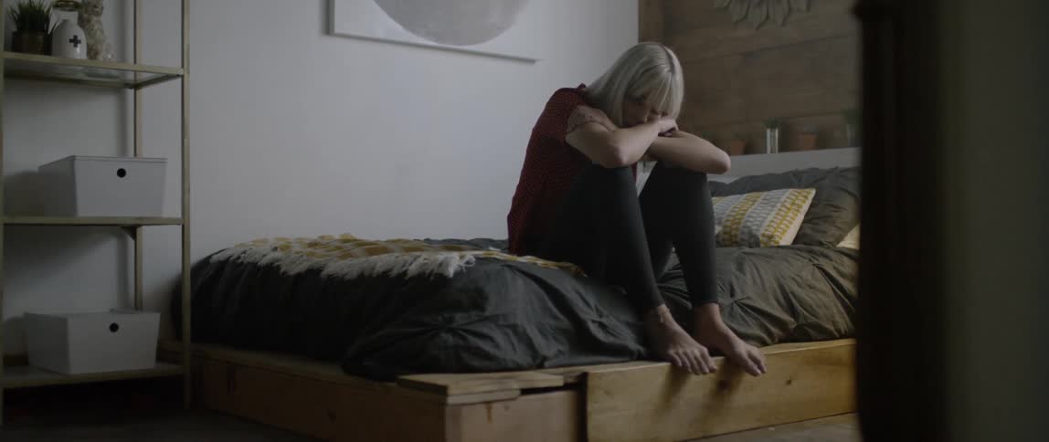 A woman is sitting in thought on her bed during the day
