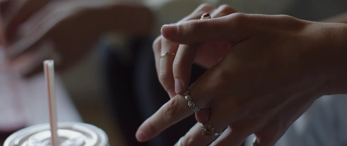 Woman's hands playing with rings near a drink