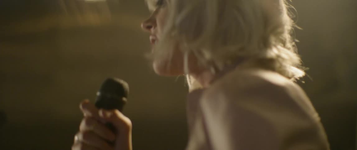 A blond woman dances and sings into a microphone