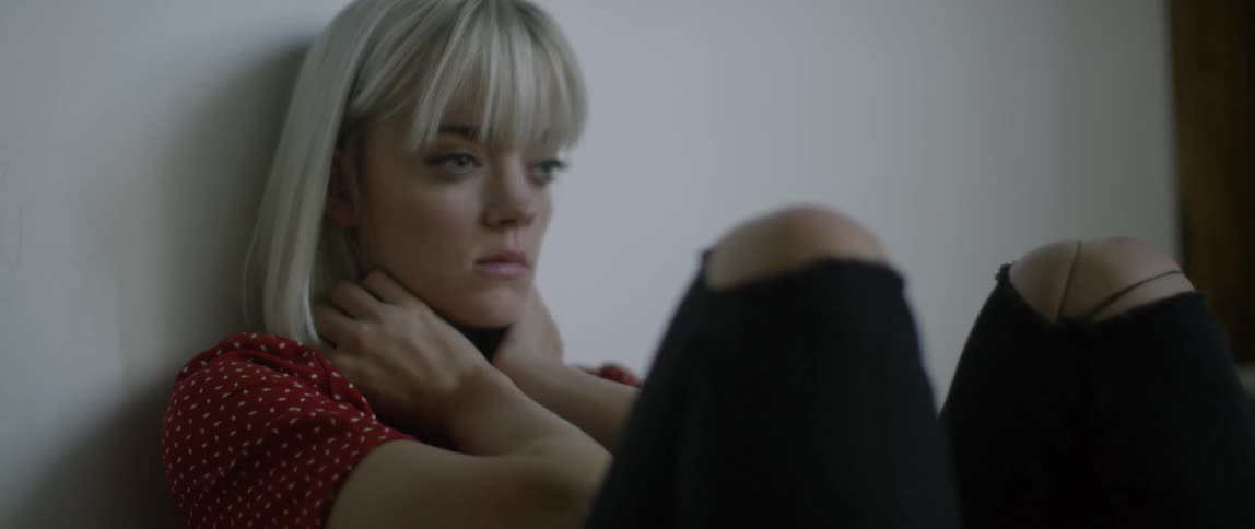 A blond haired woman sits against the wall