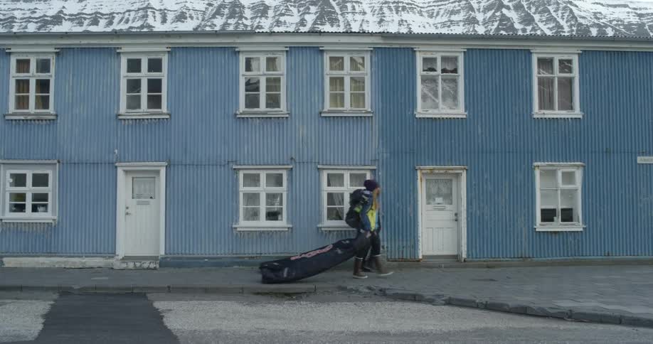People are dragging travel ski bags past an old blue building