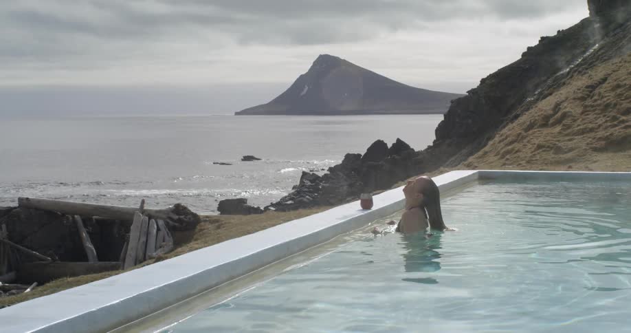 A woman is surfacing from a pool with a coastal view on a cloudy day