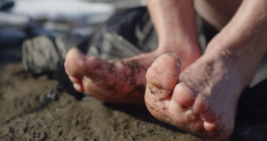 Person's cold bare toes flexing above mud on a sunny day after crossing a river