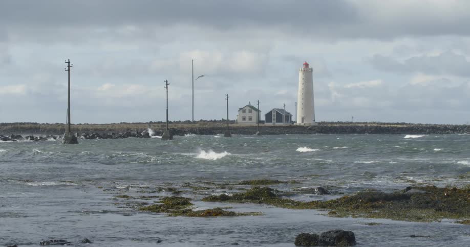 Waves are rolling onshore near a lighthouse on a cloudy day