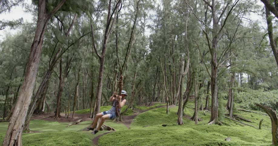 A man swings on a rope swing in a green forest