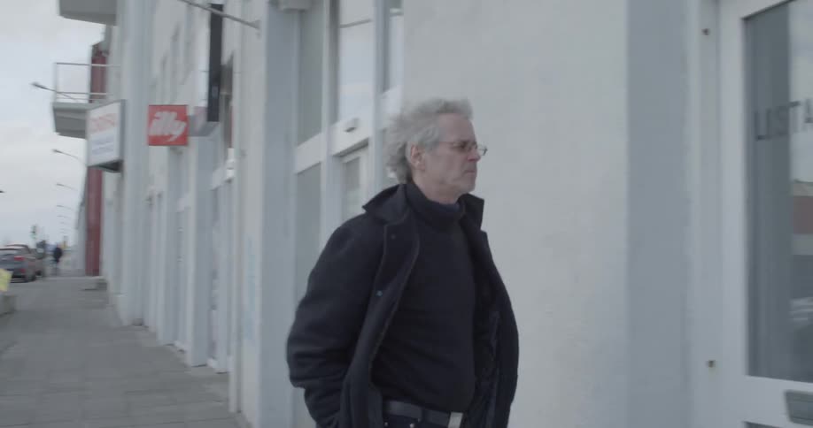 A man dressed in black walks down a city sidewalk and unlocks a door