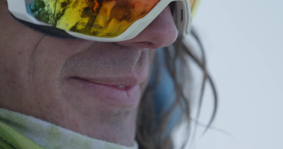 A man in ski goggles is smiling as he stands outside during the day
