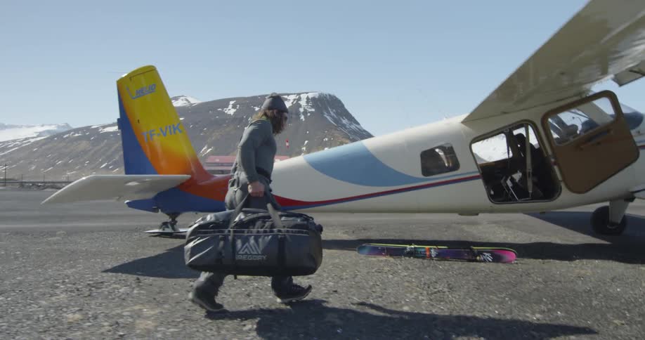 A man carries a bag toward a small plane and sets it on the ground