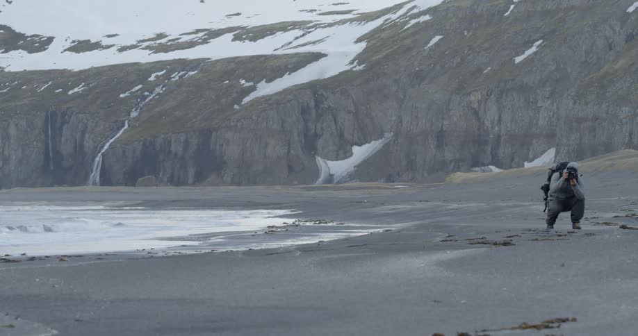 A man kneels and takes pictures on a beach