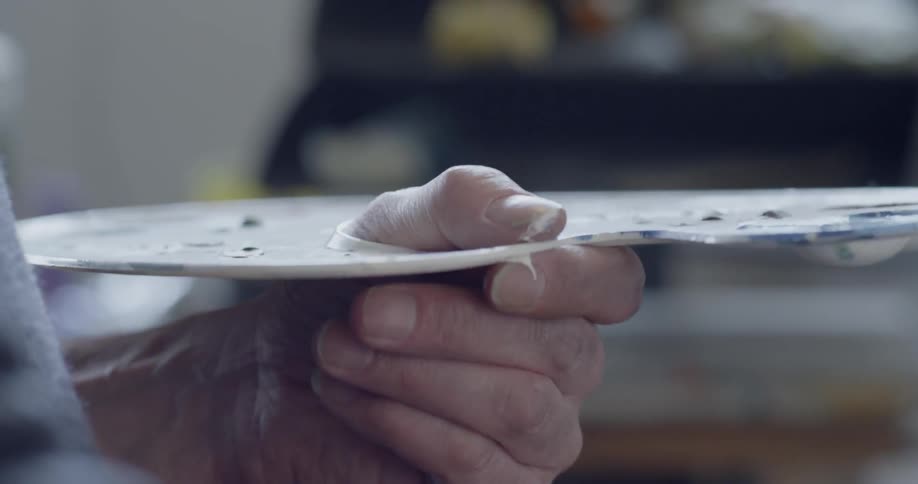An artist is holding a palette as he paints inside during the day
