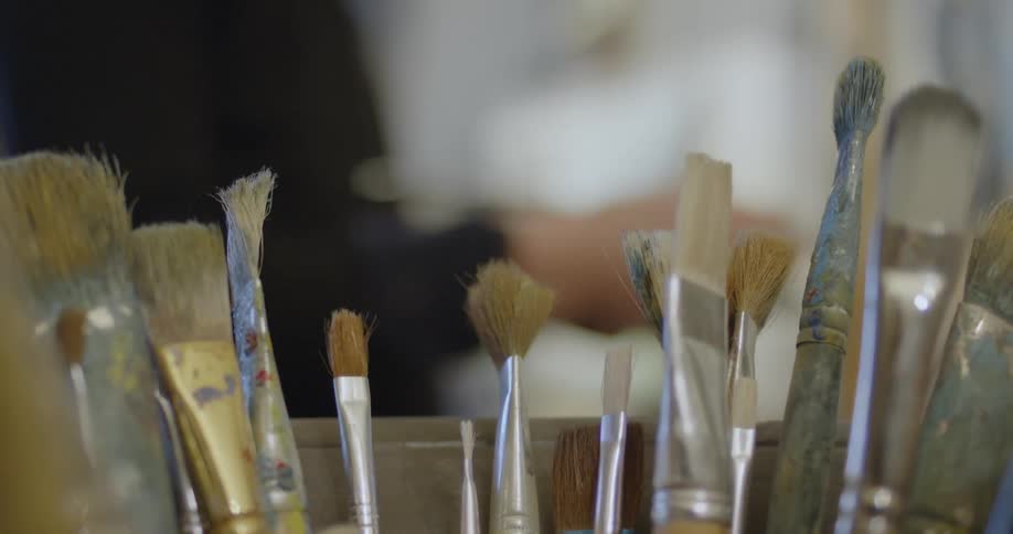 An artist grabs a paint brush from a bucket
