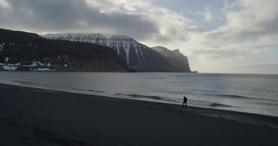 A man wearing a backpack is hiking on the beach on a cloudy day