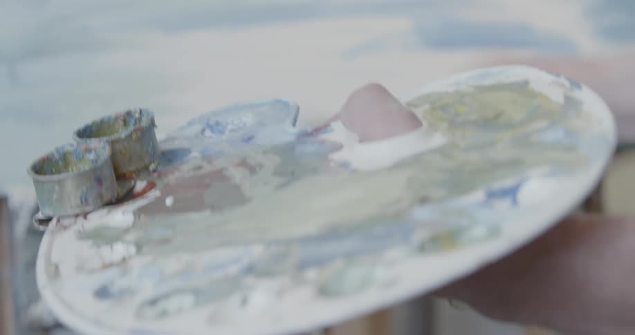 An artist dips his brush in paint on a palette
