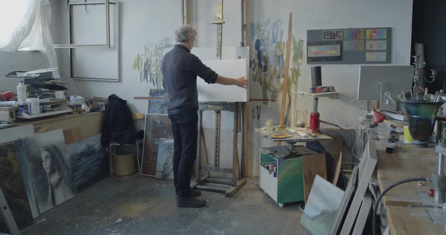 An artist lifts up a canvas and places it on an easel in studio