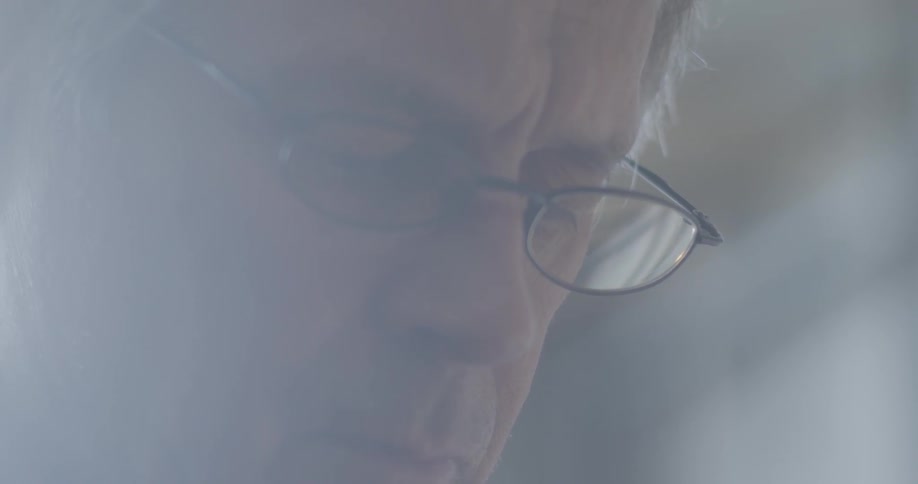 An elderly man with glasses stares downward in depression