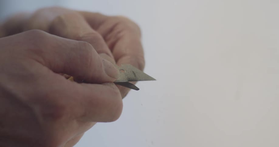 A man is using a razor blade to sharpen a charcoal pencil