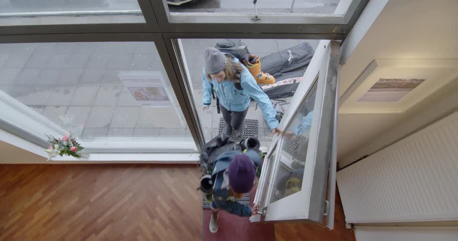 A traveling couple carrying backpacks opens a door and walks into a building