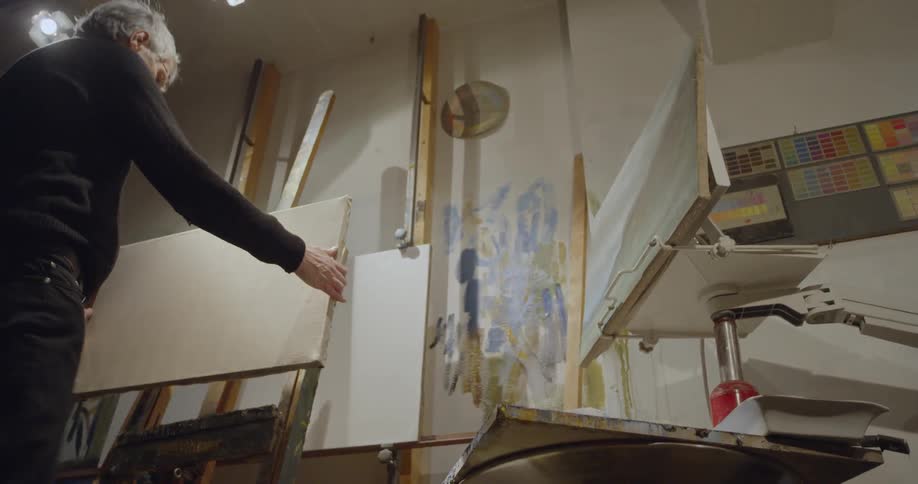 Man picks up a blank canvas and places it on an easel in a moody room
