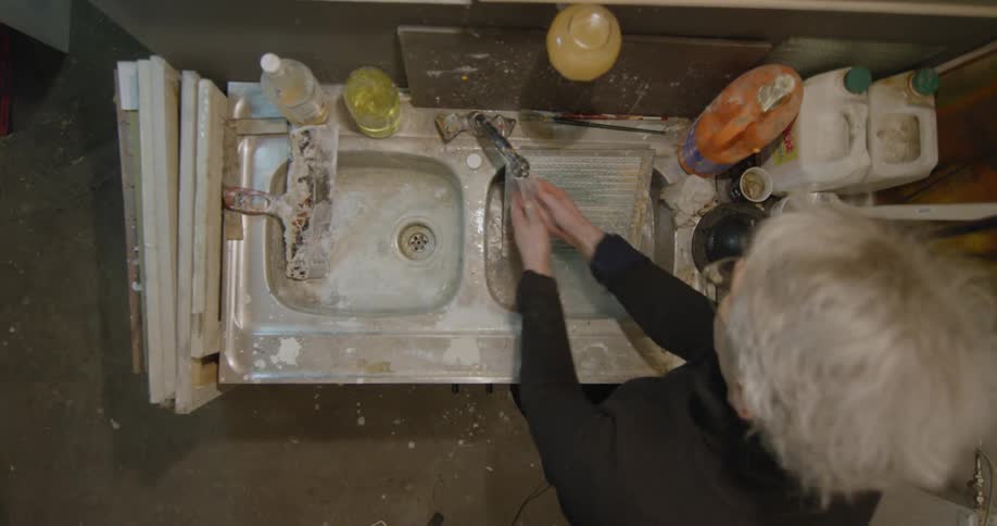 A person washes paintbrushes in a sink top down