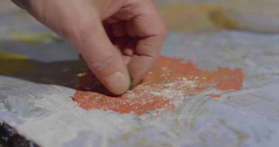An artist picks up a black piece of chalk from a painted surface
